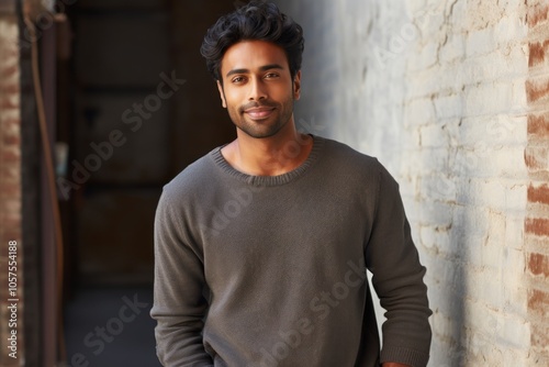 Portrait of a satisfied indian man in his 20s wearing a cozy sweater while standing against empty modern loft background