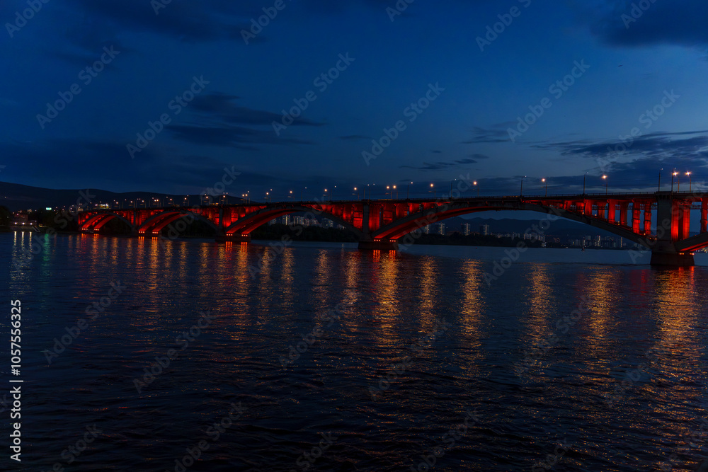 Fototapeta premium Illuminated bridge over river at dusk with reflections on wate