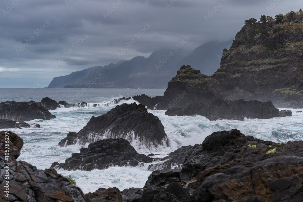 Storm clouds over rugged rock formations with a choppy ocean surf and mist along the coast of Madeira, Portugal; Seixal, Madeira, Portugal Storm clouds over rugged rock formations with a choppy ocean surf and mist along the coast of Madeira, Portugal; Seixal, Madeira, Portugal