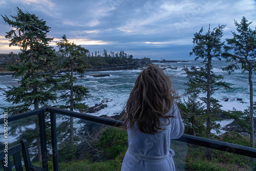 View taken from behind of a woman in a bath robe watching the never-ending ocean from a balcony in Ucluelet; Vancouver Island, British Columbia