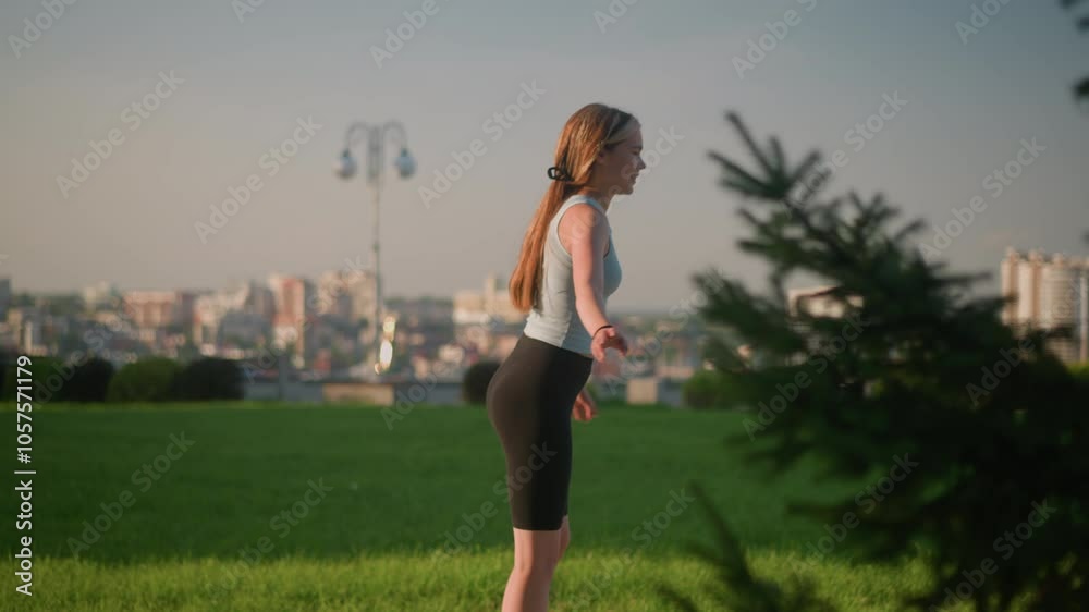 Young lady skating outdoors in sunny park, swinging her hands wide open for balance, with blurred view of cityscape and skyscrapers, background featuring lush greenery, lamp post, and trees Young lady skating outdoors in sunny park, swinging her hands wide open for balance, with blurred view of cityscape and skyscrapers, background featuring lush greenery, lamp post, and trees