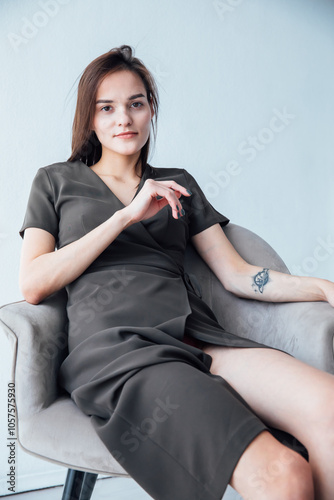 Portrait of a beautiful slender woman in a gray summer dress on an armchair