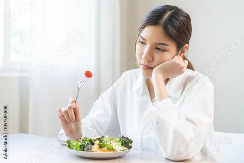 Diet in bored face, unhappy beautiful asian young woman, girl on dieting, holding fork at tomato on salad plate, dislike or tired with eat fresh vegetables. Nutrition of clean, healthy food good taste photo