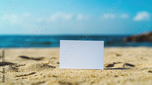 Close up of blank white paper resting on sand with a blurred ocean and sky backdrop offering space for text and messaging on a sunny day