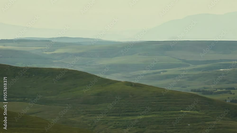 Green rolling hills extend into the distance, hazy mountains in the background Green rolling hills extend into the distance, hazy mountains in the background