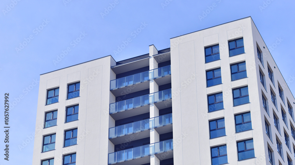 Fototapeta premium Modern high-rise apartment building in white, stand tall against a blue sky, exemplifying innovative urban architecture with sleek, angular designs.