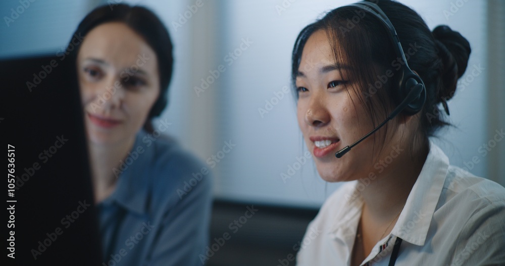 Online customer service: Close up of two female technical support operators in headsets consulting client on call, using computer. Multiethnic helpdesk specialists working in modern call center office Online customer service: Close up of two female technical support operators in headsets consulting client on call, using computer. Multiethnic helpdesk specialists working in modern call center office