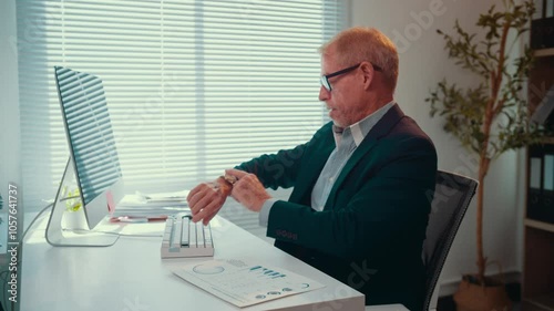 Senior businessman is working at his desk. He is typing on his keyboard, checking his watch, and then celebrating his success