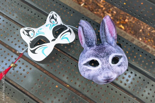 Two decorative masks, a cat and a rabbit, rest on a park bench under sunlight, showcasing intricate designs and colors, inviting curiosity from passersby. photo