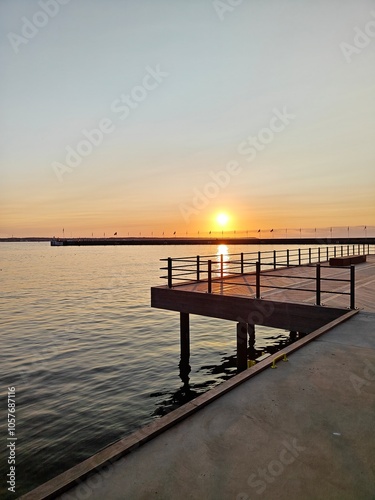 A serene sunset over the water, with a wooden pier extending into the calm sea, creating a peaceful and scenic view photo