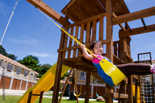 Little girl playing on a wooden swing.