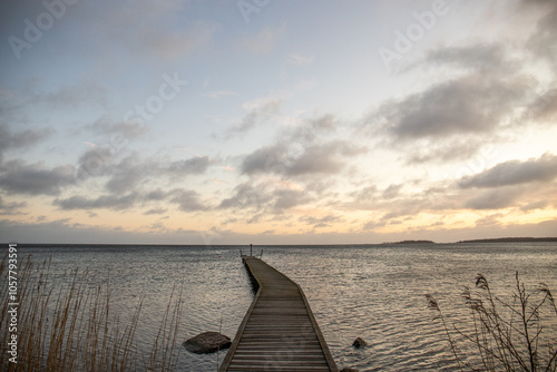 Sunrise over a lake in autumn. A wooden jetty protrudes into the water while grass has established itself on the sandy beach. The lake and beach, located on Lake Vänern in Näs Sannar, Sweden, Scandina photo