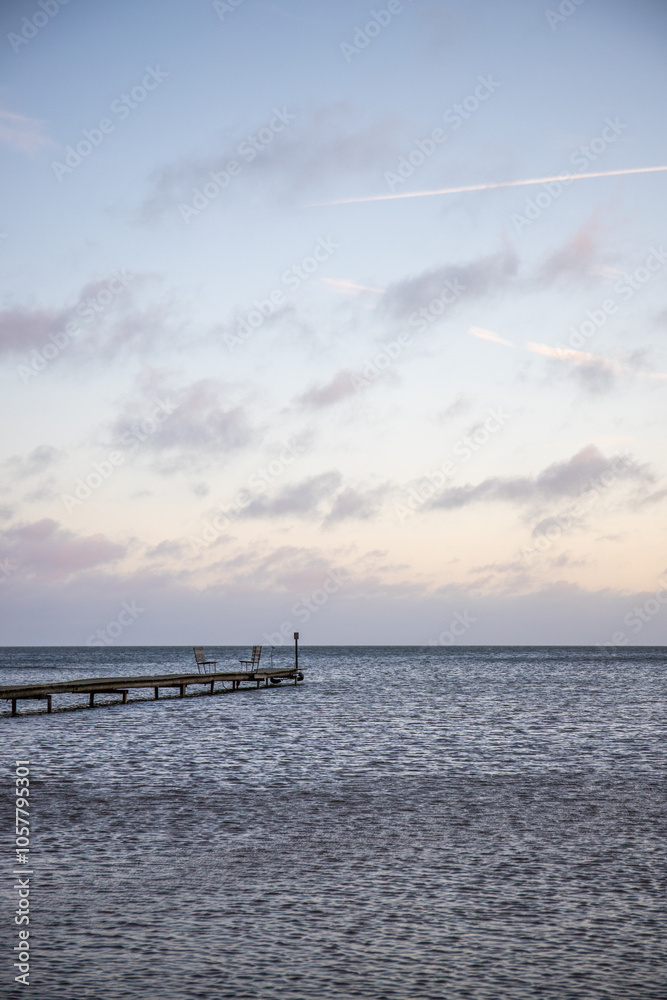 Sunrise over a lake in autumn. A wooden jetty protrudes into the water while grass has established itself on the sandy beach. The lake and beach, located on Lake Vänern in Näs Sannar, Sweden, Scandina Sunrise over a lake in autumn. A wooden jetty protrudes into the water while grass has established itself on the sandy beach. The lake and beach, located on Lake Vänern in Näs Sannar, Sweden, Scandina