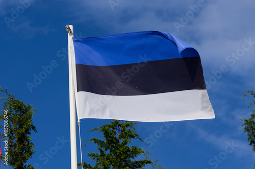 Waving Estonian flag against a clear blue sky amidst green trees in bright sunlight photo