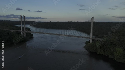 Drone drifts to the right over Oiapoque River facing bridge with sunset behind drone photo