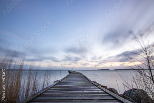 Sunrise over a lake in autumn. A wooden jetty protrudes into the water while grass has established itself on the sandy beach. The lake and beach, located on Lake Vänern in Näs Sannar, Sweden, Scandina photo