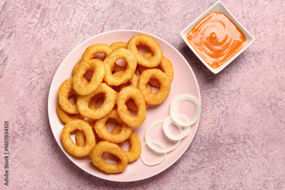 Plate with fried breaded onion rings and sauce on pink background Plate with fried breaded onion rings and sauce on pink background