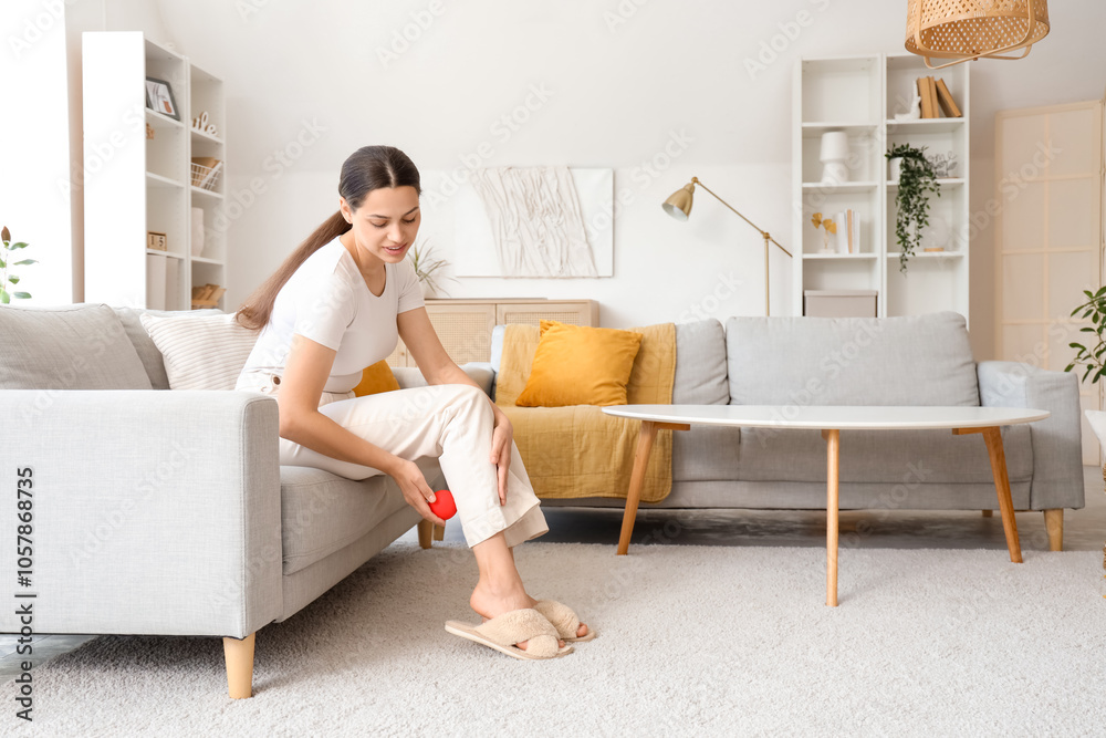 Young woman massaging her leg with ball on sofa at home Young woman massaging her leg with ball on sofa at home