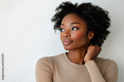 A woman with natural curly hair poses gracefully against a neutral background...