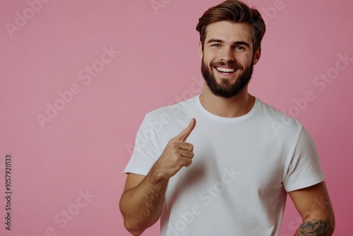 Young man smiling and gesturing to the right against a plain background in a ...