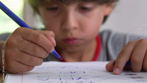 Photos Close-up of young boy intensely focused on completing a worksheet, holding a pen