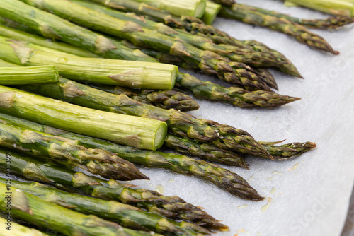 Nahaufnahme von dem im Ofen gebratenen Spargel mit Salz und Olivenöl auf dem Ofenblech mit Backpapier.