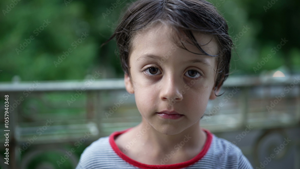 Young boy standing on a balcony, looking directly at the camera with a serious expression, quiet moment of reflection and contemplation in a natural outdoor setting Young boy standing on a balcony, looking directly at the camera with a serious expression, quiet moment of reflection and contemplation in a natural outdoor setting