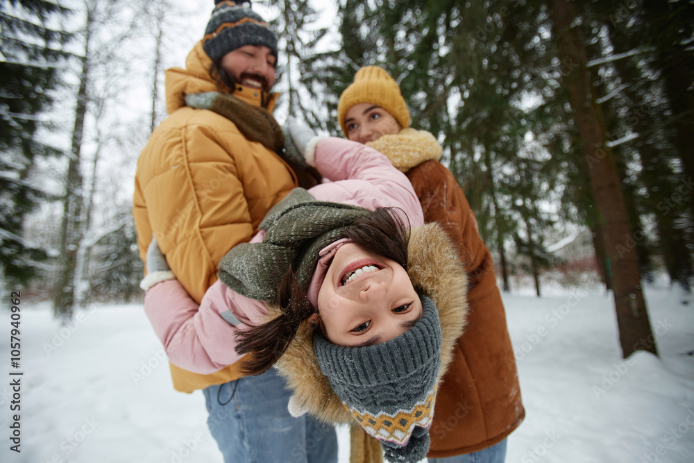 Obraz premium Portrait of happy young family playing with daughter in winter forest focus on cute girl hanging upside down in fathers arms and smiling at camera
