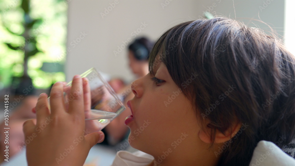 Young boy drinking water from a glass, close-up of child holding glass to mouth, focused on hydrating, quiet moment of refreshment in a relaxed home setting, natural, healthy habit Young boy drinking water from a glass, close-up of child holding glass to mouth, focused on hydrating, quiet moment of refreshment in a relaxed home setting, natural, healthy habit