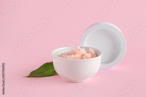 Bowl of natural body scrub and lid on pink background