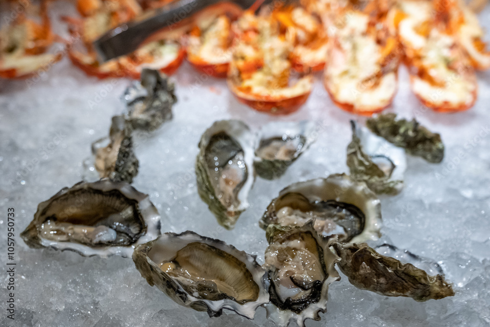 Fresh oysters on ice at a buffet, cooked lobster halves in background