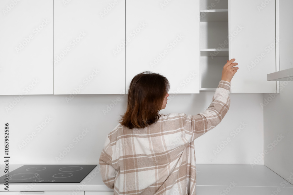 Young woman opening cupboard in kitchen, back view Young woman opening cupboard in kitchen, back view