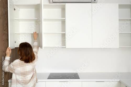 Young woman opening cupboard in kitchen, back view