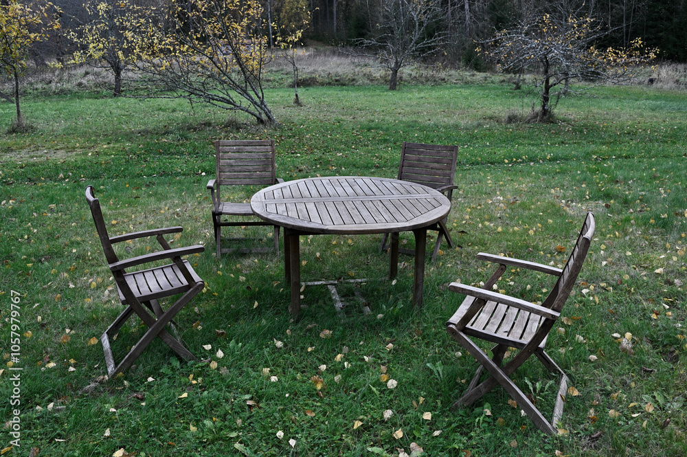 a rustic outdoor seating arrangement with a round wooden table and four wooden chairs set on green grass a rustic outdoor seating arrangement with a round wooden table and four wooden chairs set on green grass