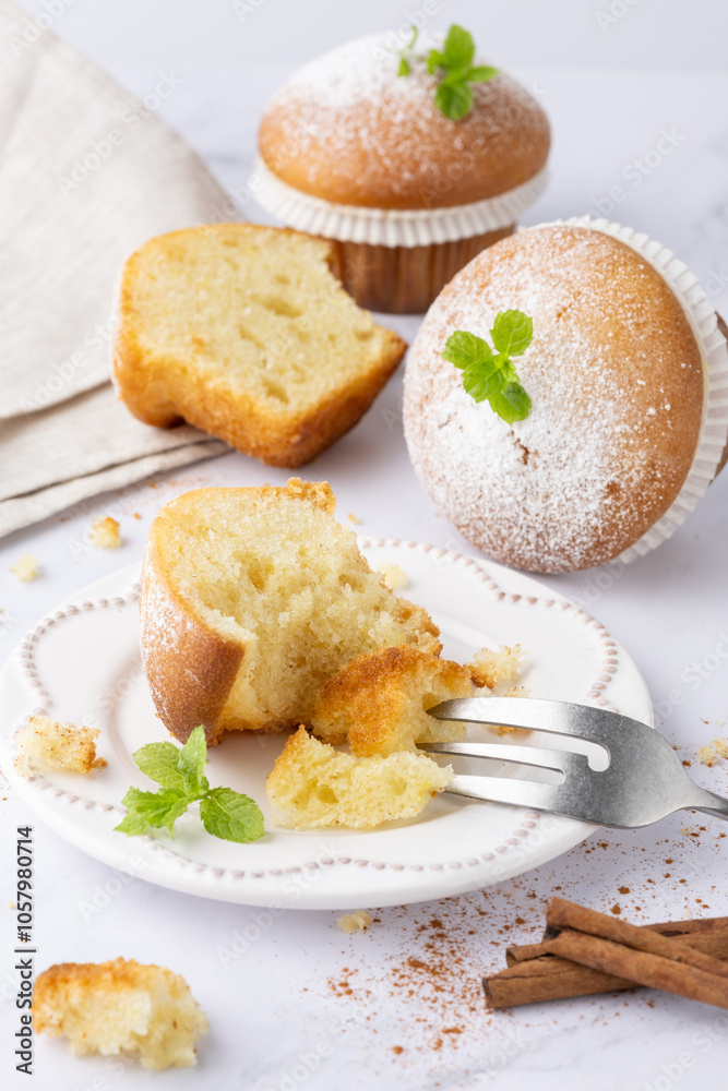 Fresh baked vanilla cinnamon bitten muffin icing sugar powder on retro plate as sweet dessert. Yummy muffins with dessert fork on light marble table Fresh baked vanilla cinnamon bitten muffin icing sugar powder on retro plate as sweet dessert. Yummy muffins with dessert fork on light marble table