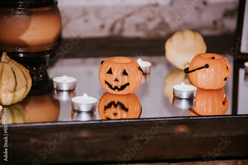 Miniature orange pumpkin buckets with jack-o'-lantern faces and tealight candles arranged on a reflective glass surface, creating a spooky Halloween ambiance.