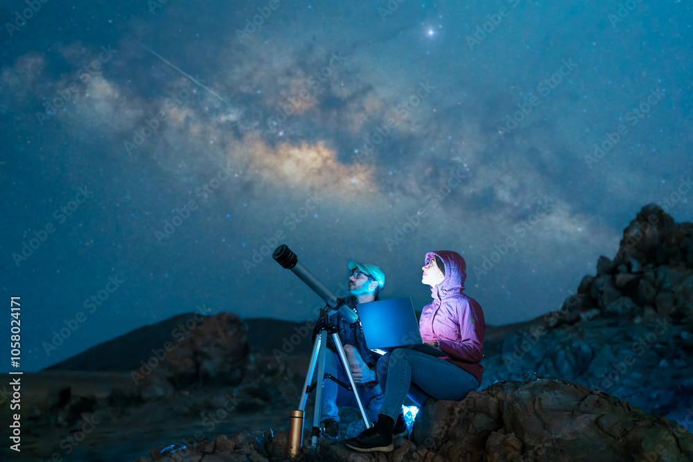 Fototapeta premium couple sitting in the desert watching the stars and Milky Way next to a telescope, stargazing and exploration concept 