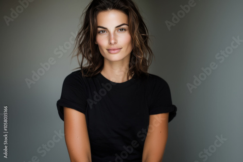 Young hispanic pretty woman smiling positively and confidently, looking satisfied and friendly. Female model wearing black t-shirt standing on neutral gray background photo