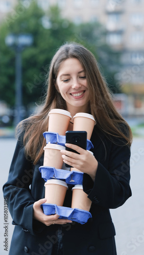 Pretty woman with long hair in office black jacket walking to work carrying many cups of takeaway coffee in her hands photo