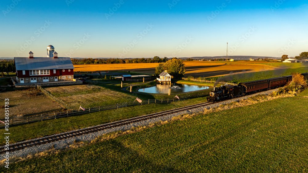 A historic steam train moves along the tracks, passing a picturesque red barn and expansive farmland. The sun sets, casting warm golden hues across the landscape, creating a serene rural atmosphere. A historic steam train moves along the tracks, passing a picturesque red barn and expansive farmland. The sun sets, casting warm golden hues across the landscape, creating a serene rural atmosphere.