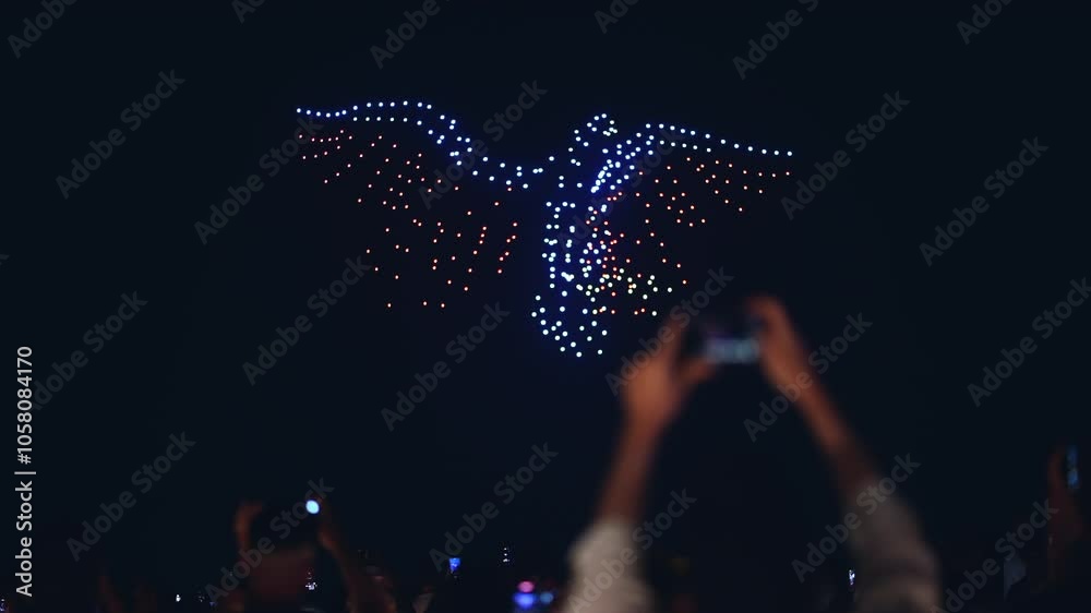 illuminated aerial drone show at glowing night sky, programmed flying robotics light performance over city, people watching and filming, advanced technology concept