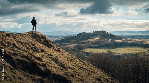 Pilgrim reflecting on scenic hill overlooking vast countryside with distant castle