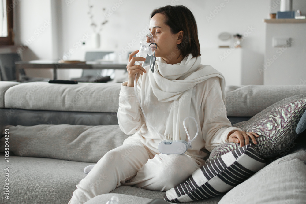 Sick Woman Is Using A Nebulizer For Inhalation At Home While Sitting On A Sofa Sick Woman Is Using A Nebulizer For Inhalation At Home While Sitting On A Sofa