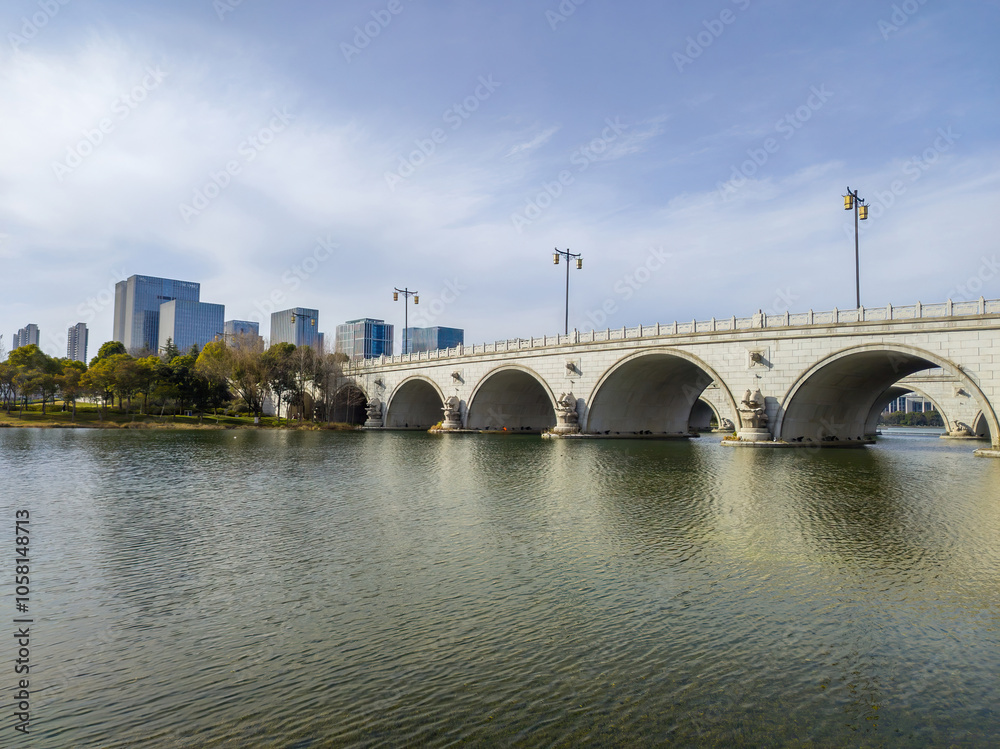 Fototapeta premium Serene Urban Bridge Over Calm Waters with City Skyline Background