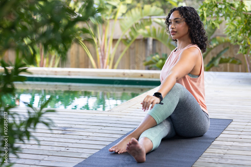 Woman practicing yoga on mat by pool, enjoying peaceful outdoor setting