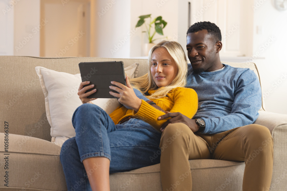 multiracial couple relaxing on couch, watching tablet together at home, feeling cozy multiracial couple relaxing on couch, watching tablet together at home, feeling cozy