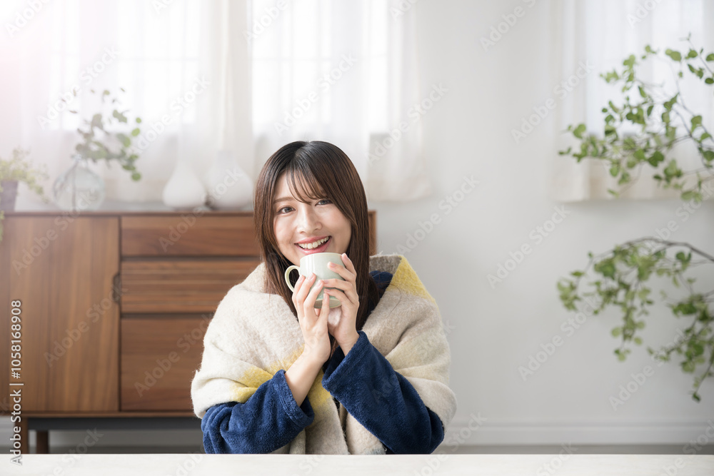 冬のリビングで温かい飲み物を飲むくつろぐ若い女性 カメラ目線の笑顔 冬のリビングで温かい飲み物を飲むくつろぐ若い女性 カメラ目線の笑顔
