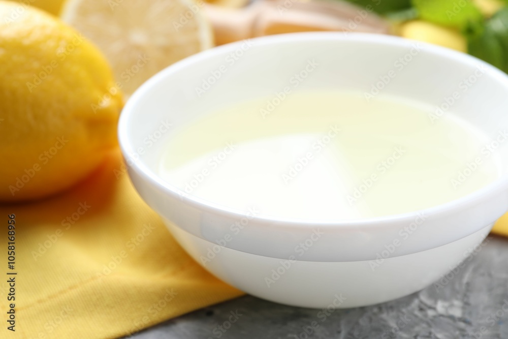 Fresh lemon juice in bowl and fruit on grey table, closeup Fresh lemon juice in bowl and fruit on grey table, closeup