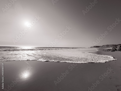 Fotografie Low angle view of waves washing up onto beach with sun reflecting back on the we