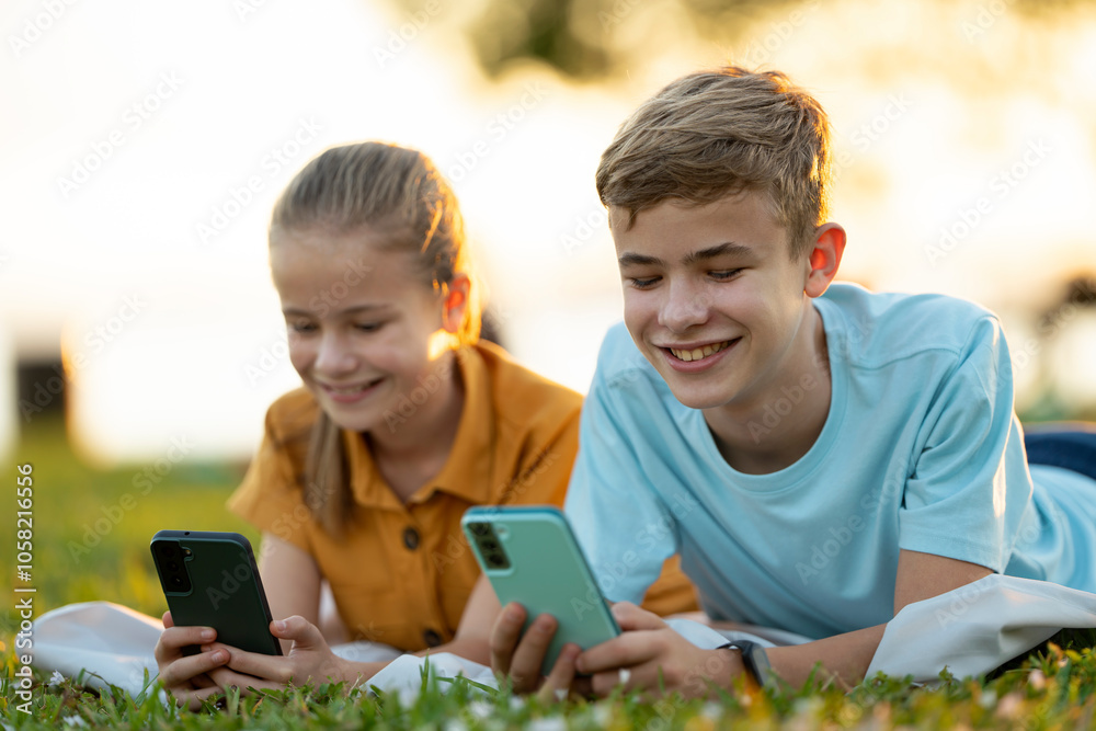 Positive children messaging on their mobile phones with friends outdoors in summer park.
